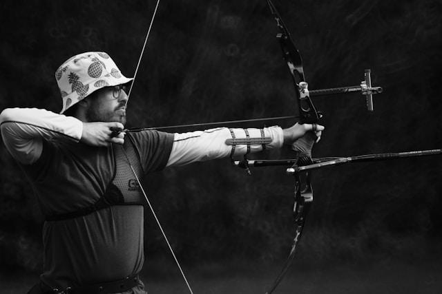 A black and white image of a man pulling a bow taut with the arrow cocked.