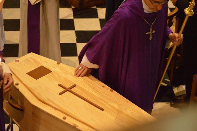 A priest with his hand on a wooden coffin.