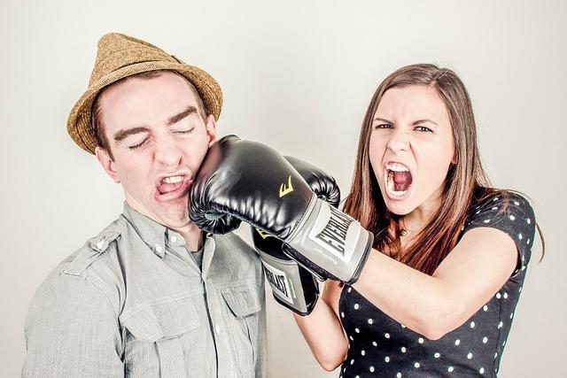 A woman hitting a man in the cheek with a boxing glove while obviously yelling something.