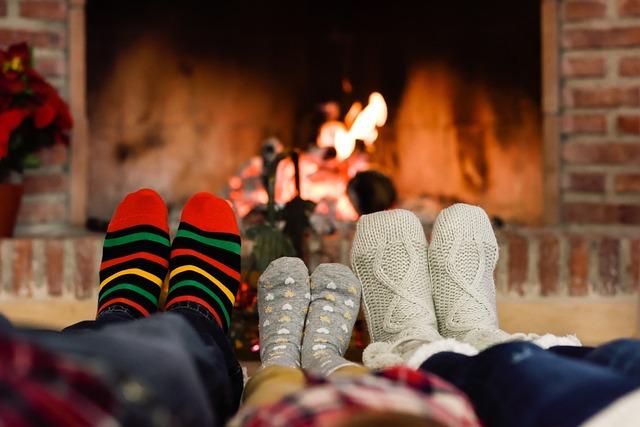 Three pairs of sock feet in front of a cozy fireplace.