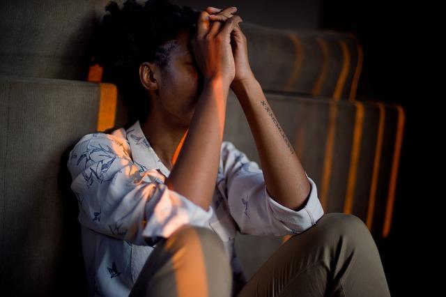 Person sitting on the floor with their back against the wall, knees up, elbows resting on knees, hands in front of their face.