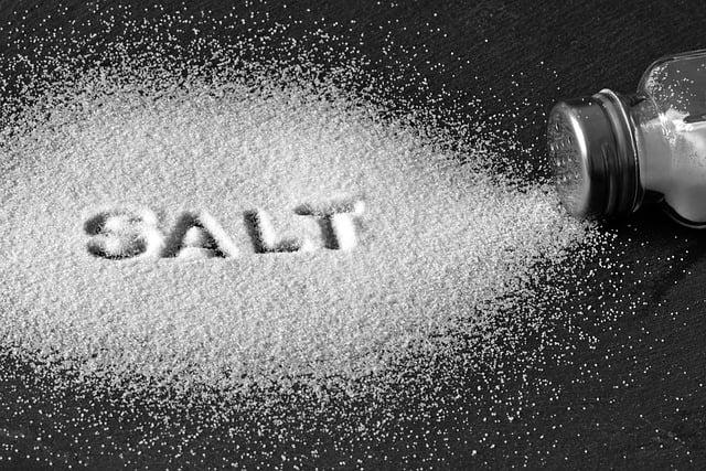 A salt shaker tipped over with the word 'salt' written in the spilled grains of salt.