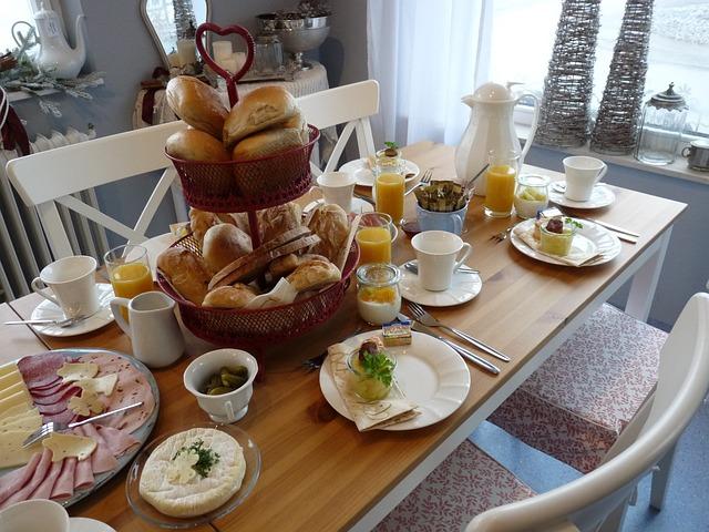 wood table with white chairs set for a lunch with buns, cold cuts and tea.