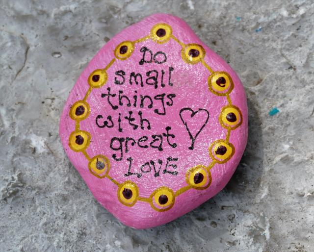 A rock painted pink with the words Do small things with great love.