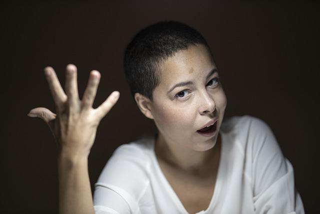 A surprised woman, hand in the air, mouth open with a black background.