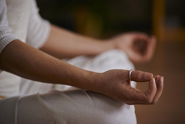 A close up of the hands and legs of a person in a yoga lotus-pose position.