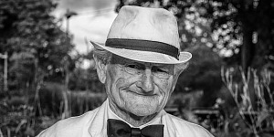 Black and white photo of a very old man dressed in white with a white hat and bow tie.