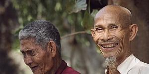 Two south Asian men sitting under a tree laughing.