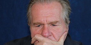 Head shot of a man in his late fifties with a receding hairline, worried eyes, and one hand covering his mouth as he thinks.