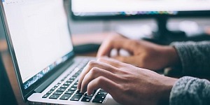 A side perspective of an open laptop with hands typing at the keyboard.