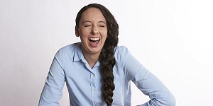 A woman standing with her hands at her middle, bent over laughing hilariously.