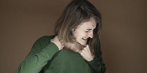 A woman with a green sweater, pulling at the neckline, looking away in pain.