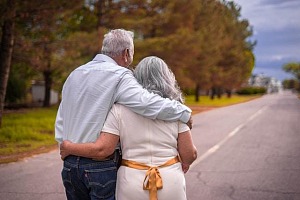 Elderly couple walking with an arm around one another down a quiet country road.