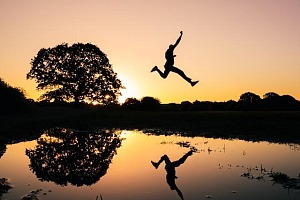 silouette of person jumping across a pond with their reflection below