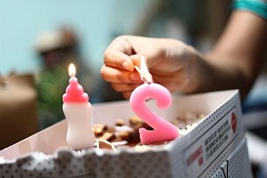 A hand holding a match lighting a pink 2 on a birthday cake.