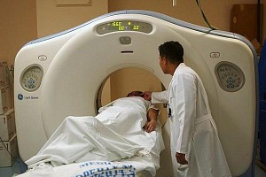 MRI machine with a doctor standing beside a patient who is being scanned.