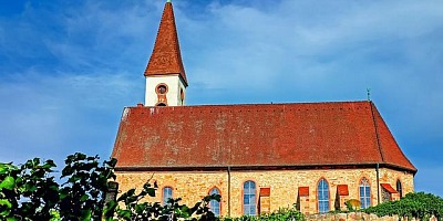 A moderate sized church building, with yellow brick walls, a red roof and a blue sky with wispy clouds.